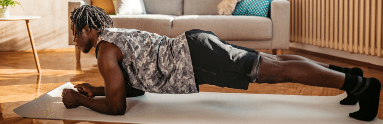 Young handsome man workout in his living room on yoga mat exercising plank position.