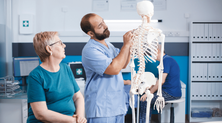 Nurse and retired patient looking at spinal cord on human skeleton for osteopathic examination