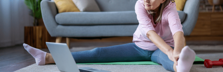 Mature woman practicing yoga at home using laptop