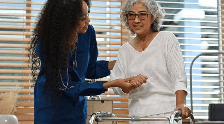 An African Physical therapist or Caregiver help and support the old stroke patient woman standing with a walker at home